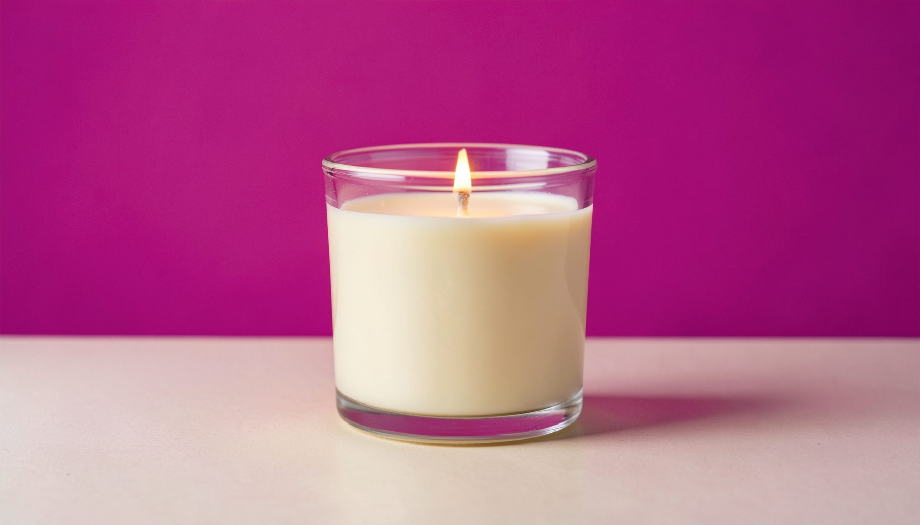 A softly lit soy candle in a clear glass jar on a neutral surface, warm cream and blush tones, calm and serene mood.